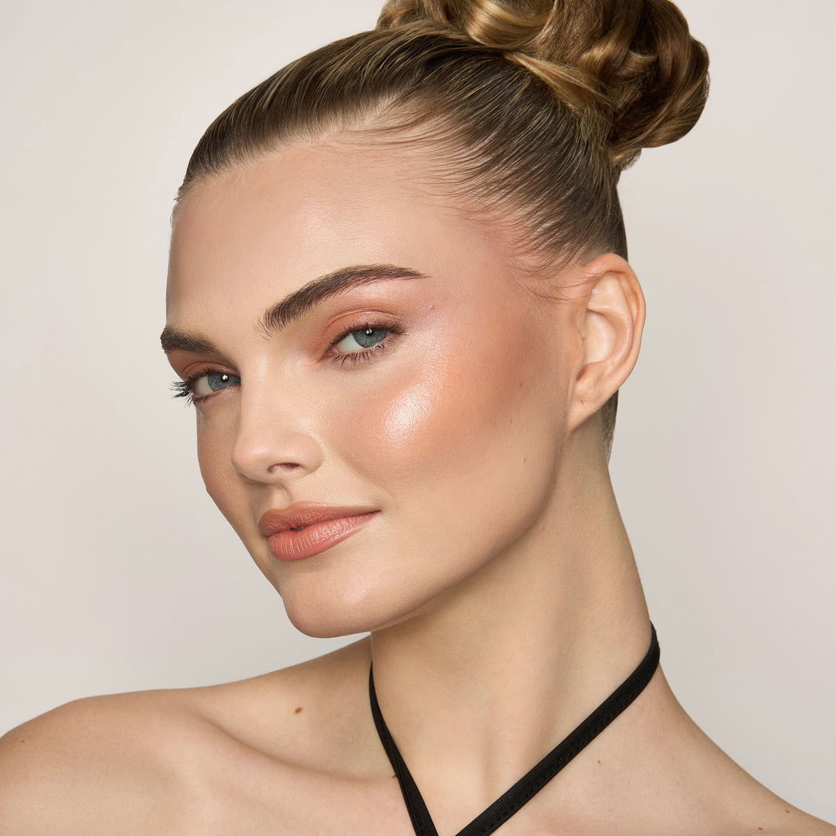Eine Frau mit hellem Hautton präsentiert den Yummy Skin Blurring Balm Powder Lowlighter Lowkey vor einem schlichten Hintergrund.
