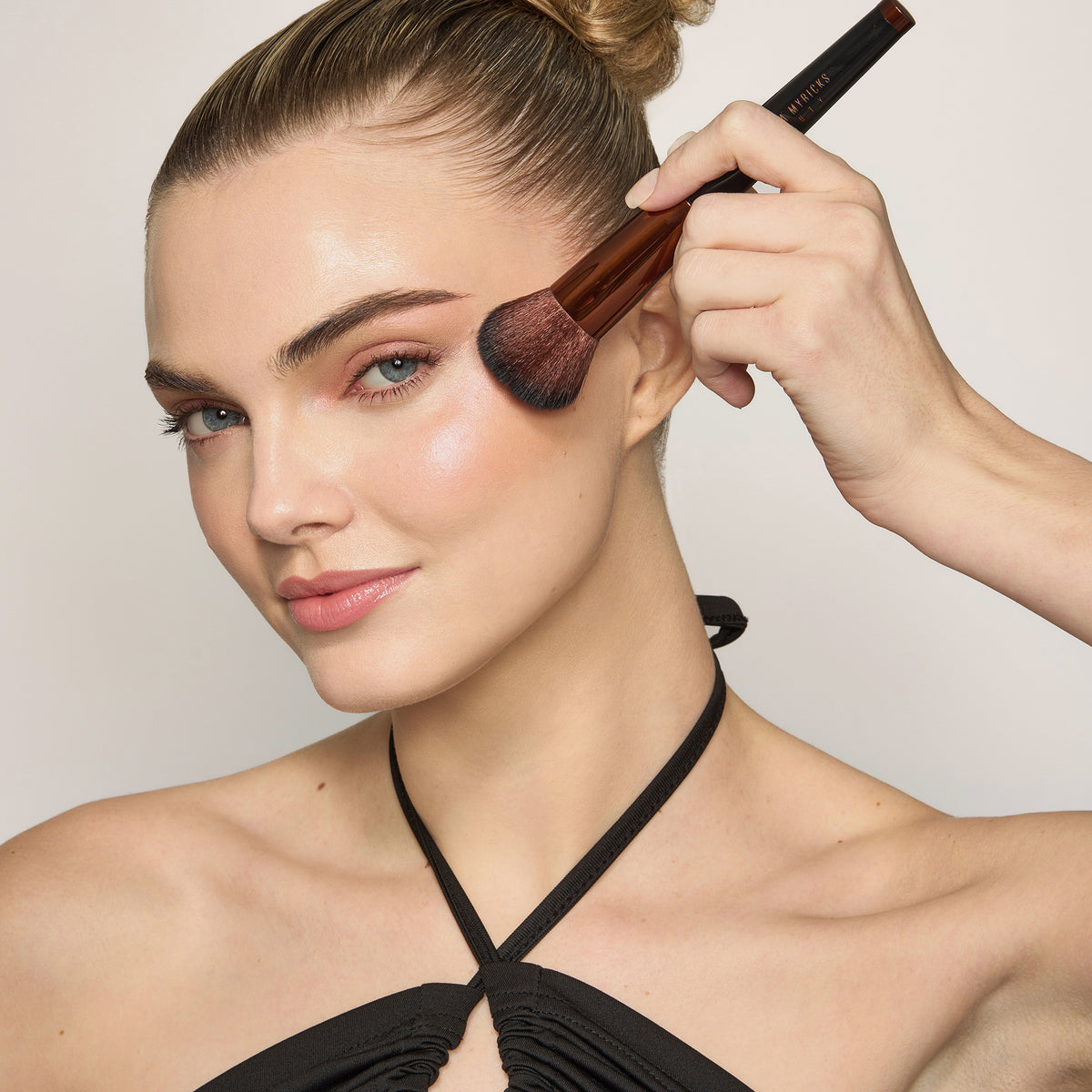 Eine Frau trägt den Yummy Skin Blurring Balm Powder Lowlighter Unbothered mit einem Make-up-Pinsel auf ihre Wange.
