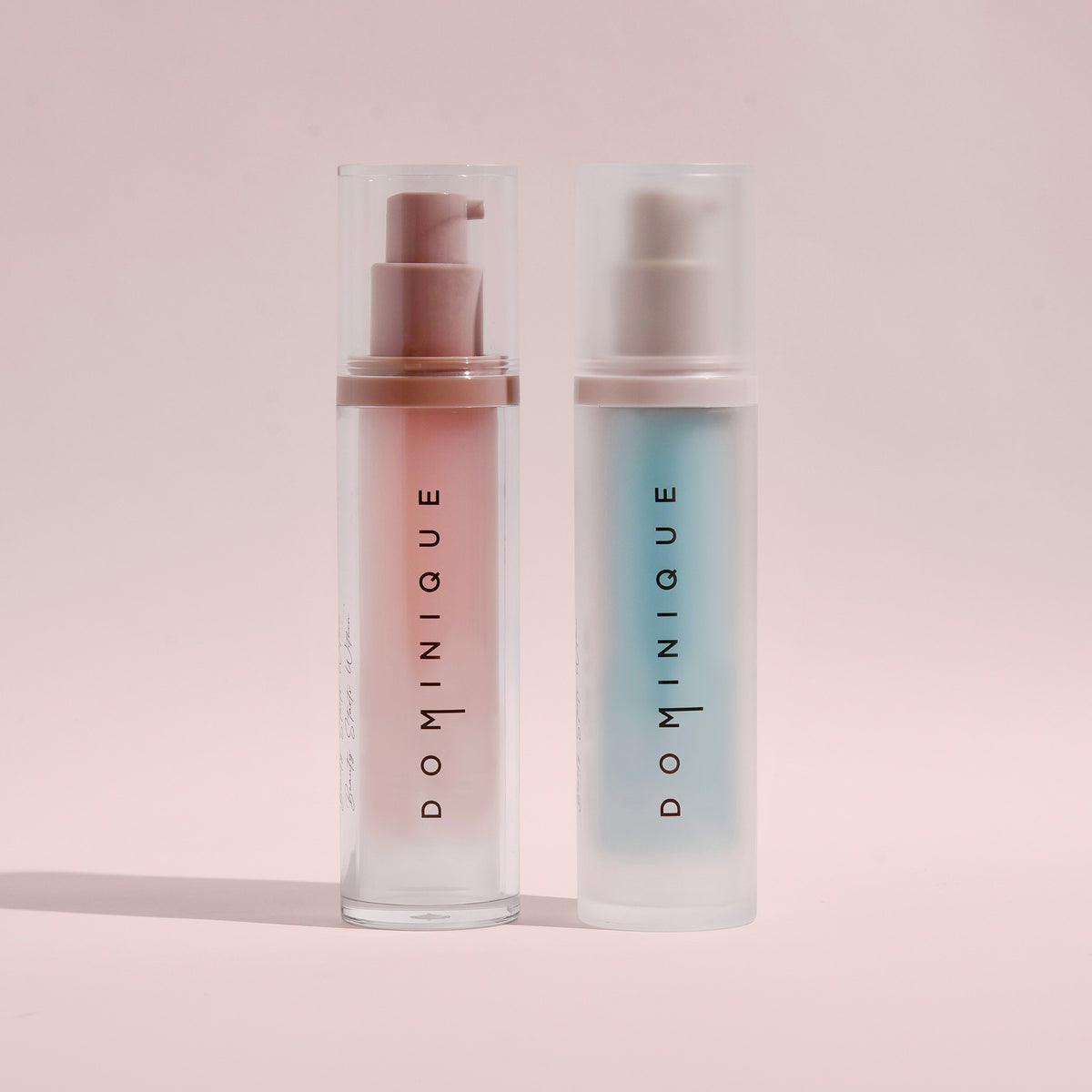 Zwei Dominique Moisture Grip Serum Primer-Flaschen mit Pumpspender, eine mit rosa Flüssigkeit und eine mit blauer Flüssigkeit gefüllt.