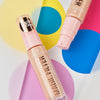 Zwei Flaschen MAGIC FILTER Glow Booster 10 Light liegen auf einem bunten geometrischen Hintergrund.
