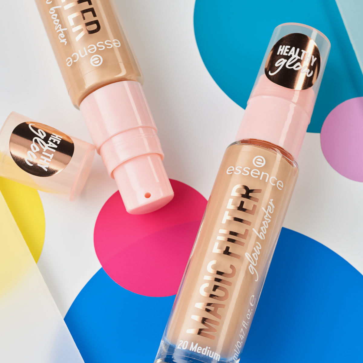 Zwei Flaschen MAGIC FILTER Glow Booster 20 Medium liegen auf einem bunten geometrischen Hintergrund.
