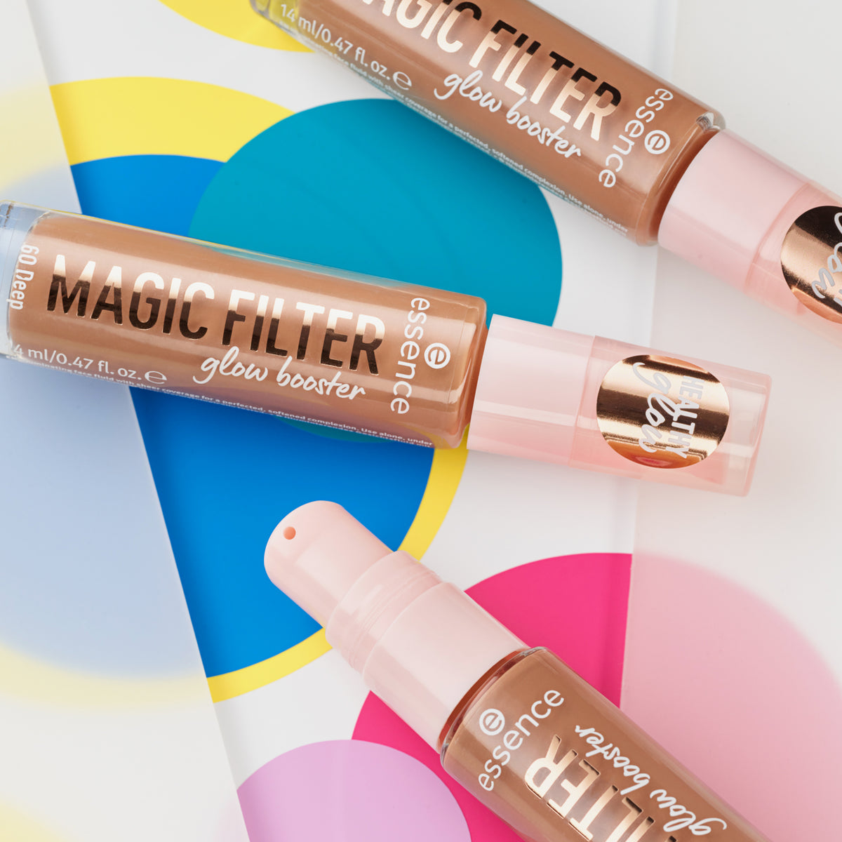 Drei Flaschen MAGIC FILTER Glow Booster 60 Deep liegen auf einem bunten geometrischen Hintergrund.