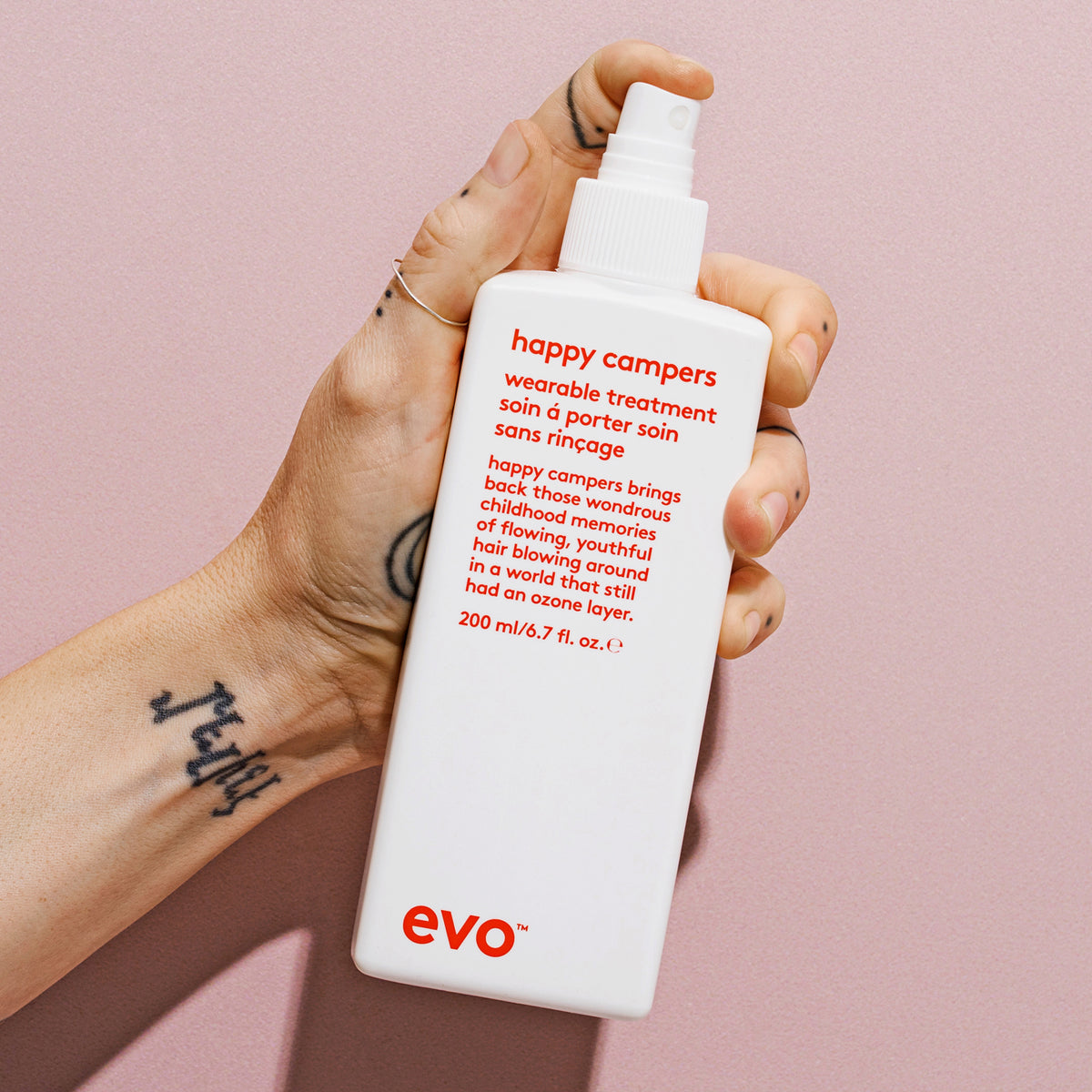 Eine Hand hält eine weiße Flasche Happy Campers Wearable Treatment vor einem hellen Hintergrund.
