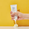 Eine Hand drückt vor einem leuchtend gelben Hintergrund eine Tube Seven Layer Ceramide Cream aus.
