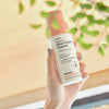 Hand hält eine Flasche Vitamin C Glow Powder Cleanser in der Nähe von grünen Blättern und Sonnenlicht.