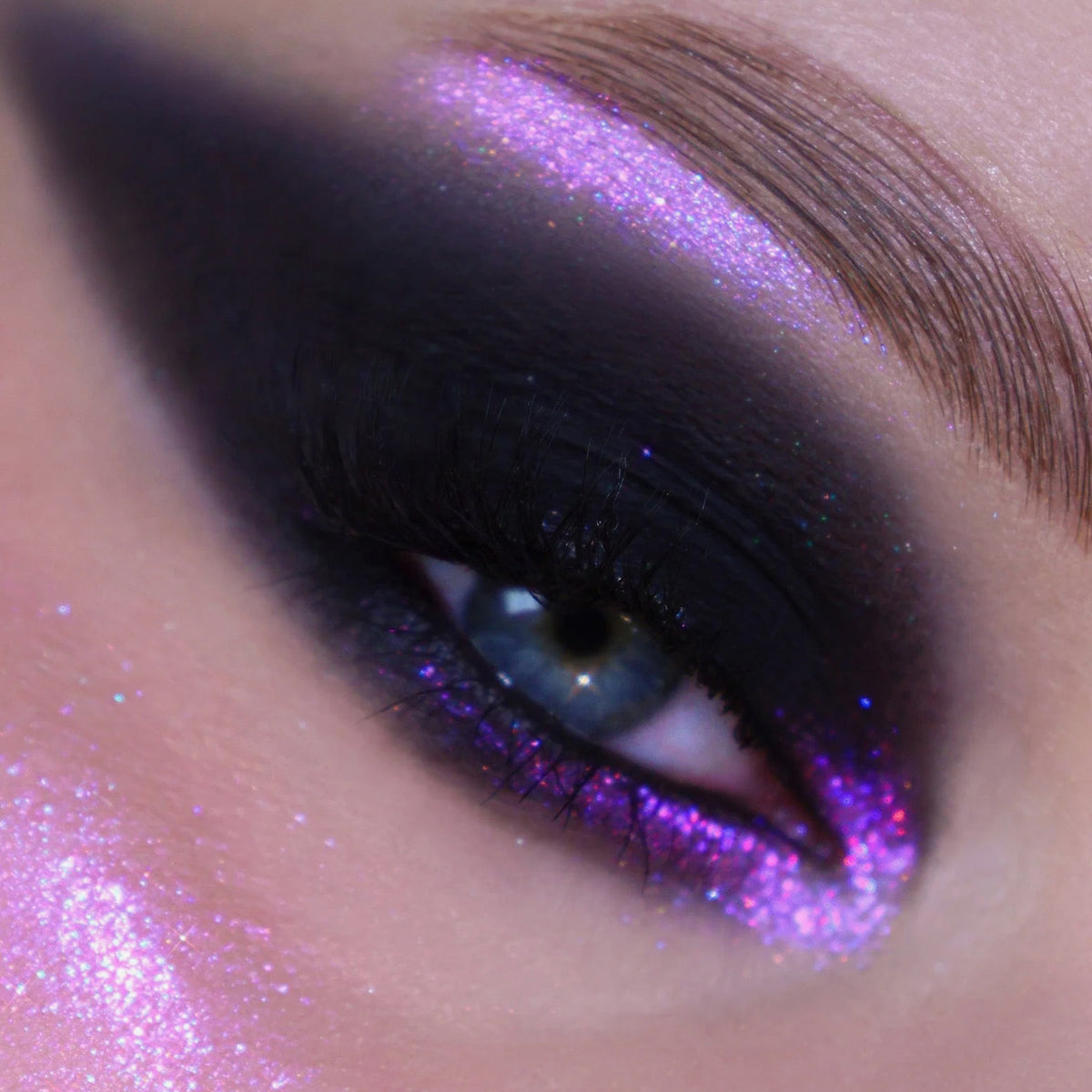 Nahaufnahme eines Auges mit dramatischem schwarzem Moonshadow Matte Pressed Eyeshadow und violettem Glitzer.
