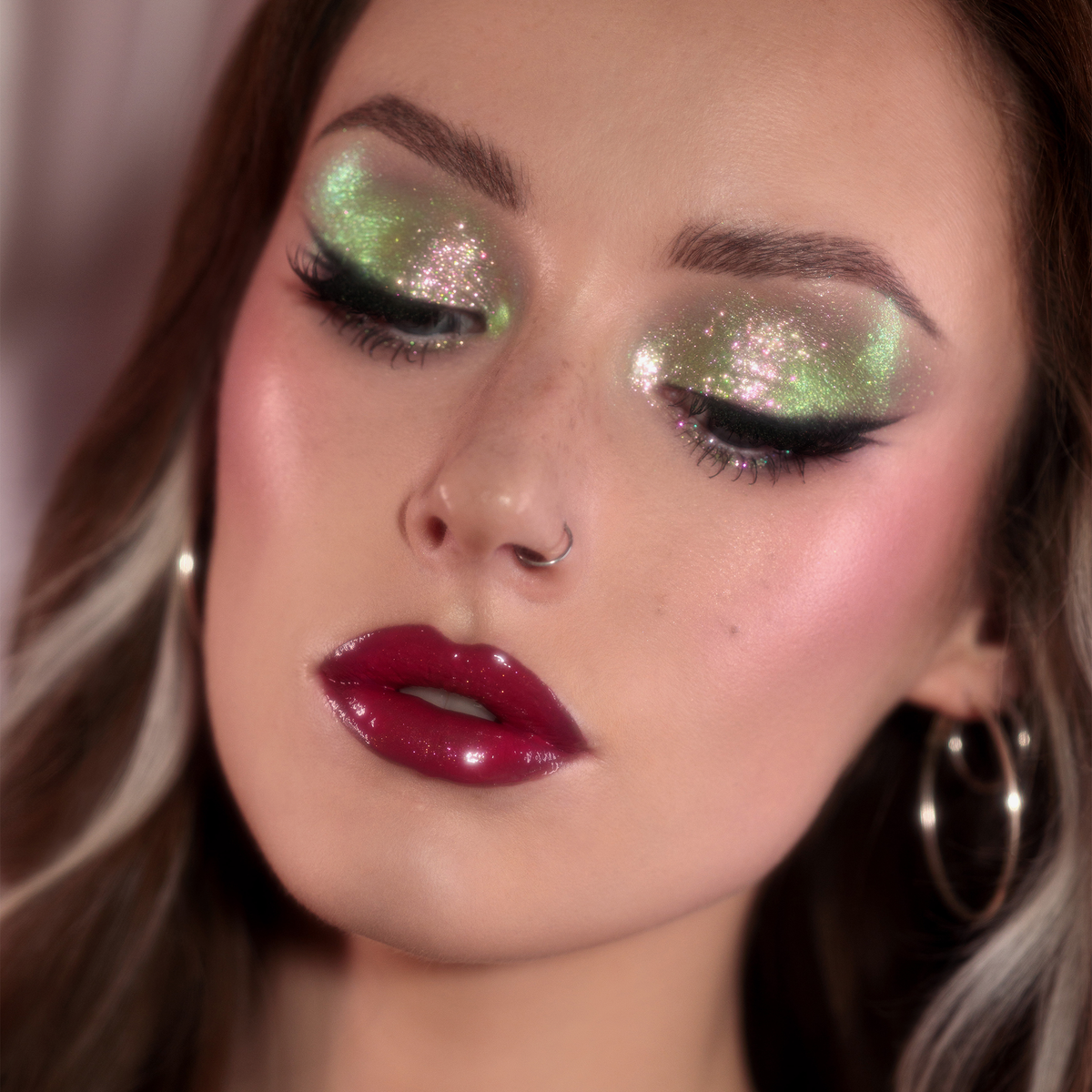 Frau mit dramatischem Eyeliner und glänzenden dunkelroten Lippen trägt grün schimmernden Opal Moonstone Loose Multichrome Eyeshadow in Lucky Charm auf den Augen.