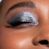 Ein geschlossenes Auge, geschminkt mit schimmerndem silbernen Lidschatten aus der Aim Higher-Palette von LH Cosmetics und langen, geschwungenen Wimpern.