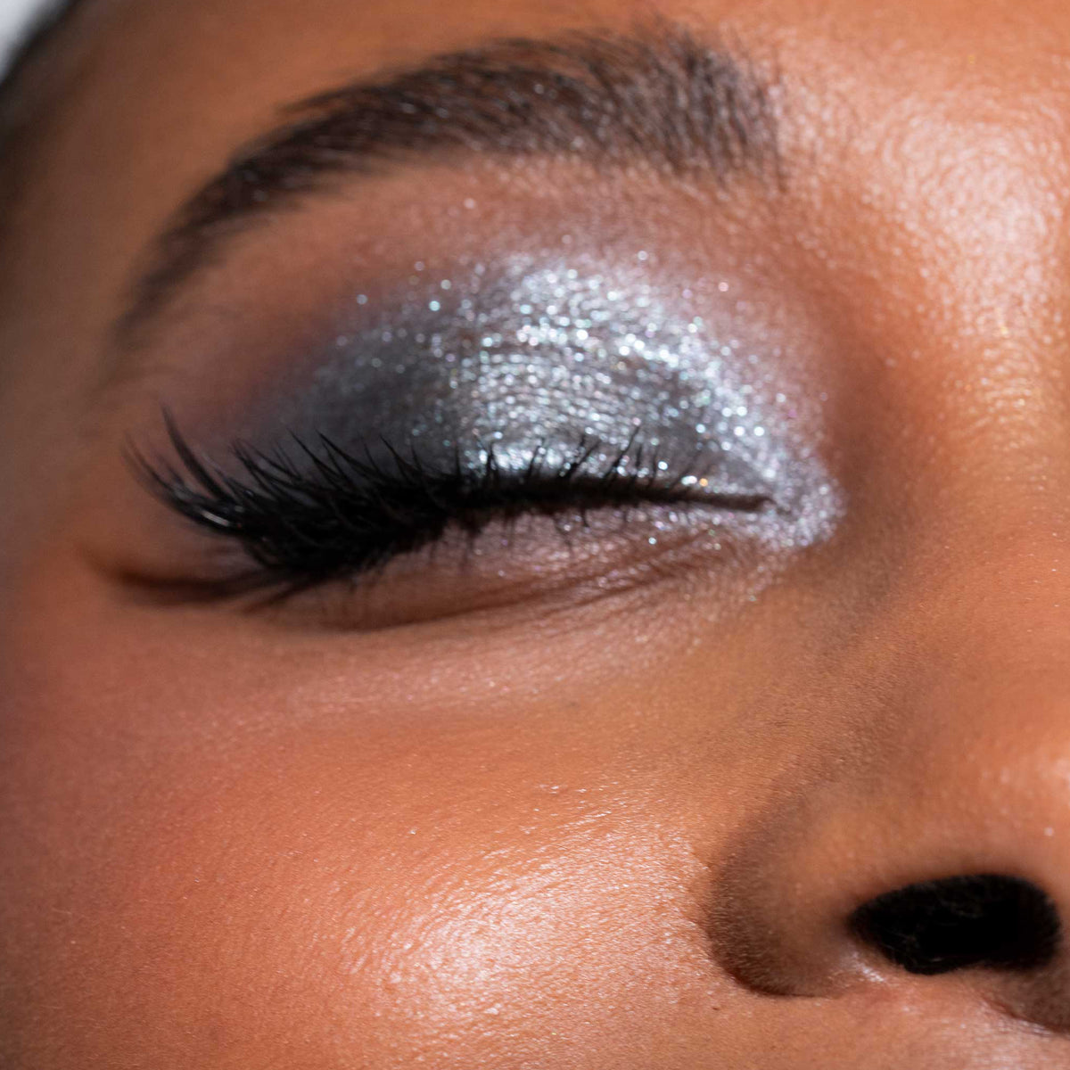 Ein geschlossenes Auge, geschminkt mit schimmerndem silbernen Lidschatten aus der Aim Higher-Palette von LH Cosmetics und langen, geschwungenen Wimpern.