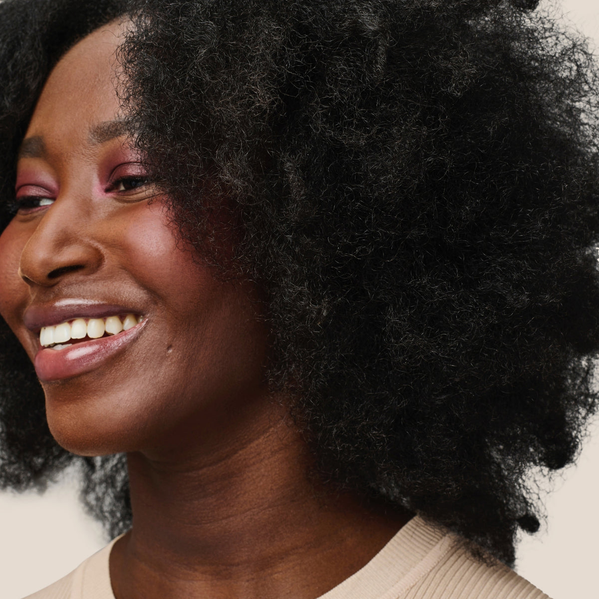 Frau mit natürlich lockigem Haar, gestylt mit Living Proof Curl Elongator, lächelt vor einem hellen Hintergrund.