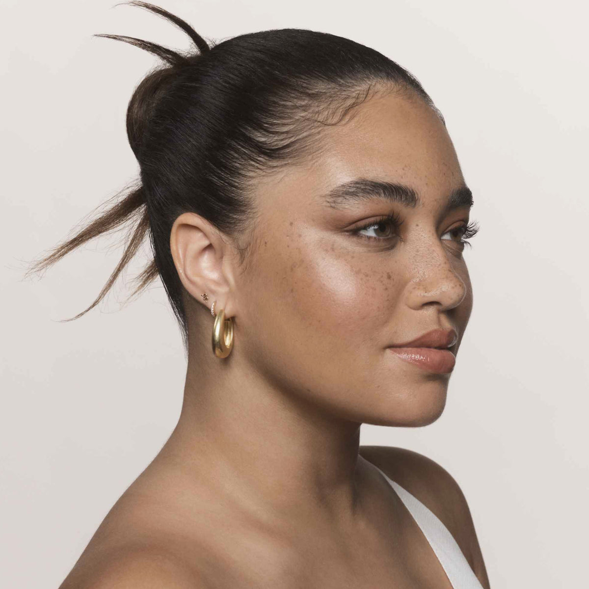Eine Frau mit zurückgekämmtem Haar präsentiert das No Frizz Smooth Styling Serum von Living Proof.