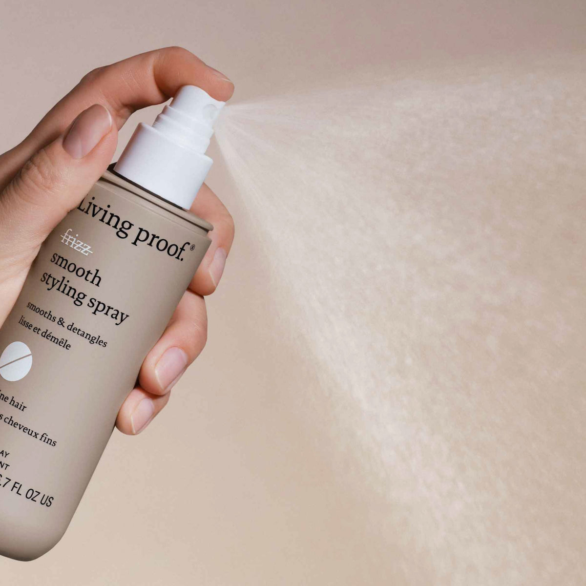 Eine Hand sprüht Living Proof No Frizz Smooth Styling Spray; der Nebel ist vor einem neutralen Hintergrund sichtbar.