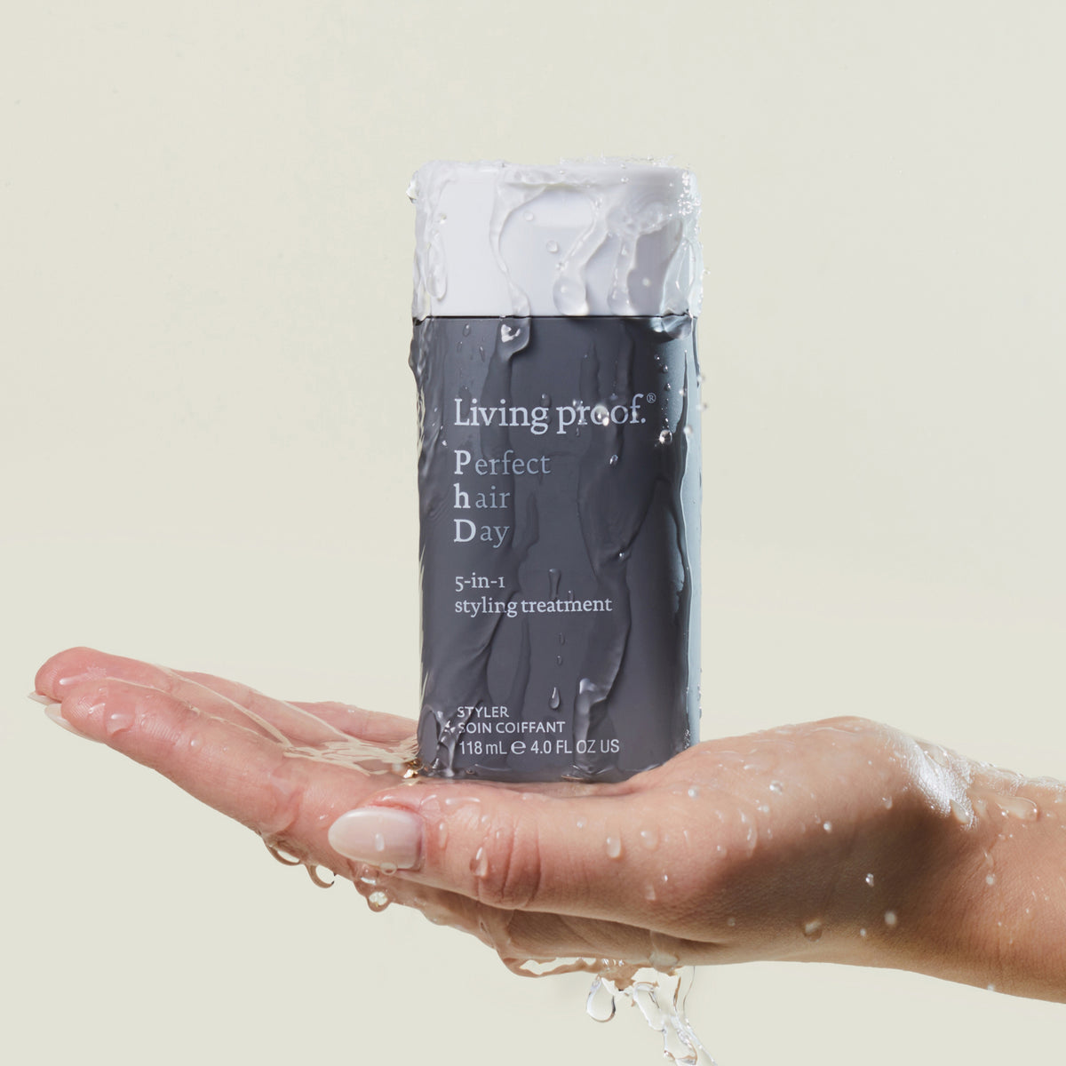 Eine nasse Hand hält eine Flasche Living Proof Perfect Hair Day 5-in-1 Styling Treatment vor einem hellen Hintergrund.
