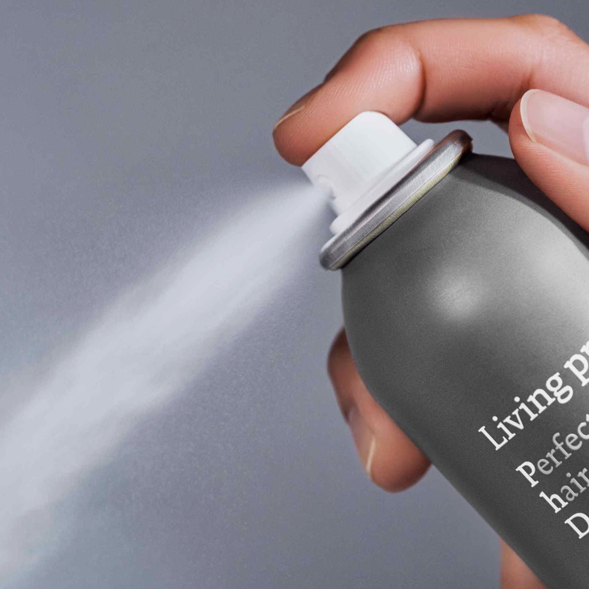 Eine Hand drückt auf die Düse einer Dose Living Proof Perfect Hair Day Dry Shampoo, wodurch ein feiner Nebel freigesetzt wird.