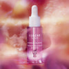 Ein Tropffläschchen von Lumene NORDIC BLOOM [LUMO] Vegan Collagen Essence steht vor einem sanft verschwommenen floralen Hintergrund.