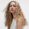 Eine blonde Frau Haar präsentiert langes, lockiges Haar nach Anwendung des Sheer Silver Shampoo von maria nila.