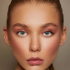 Nahaufnahme einer Frau mit blauen Augen, glänzenden Lippen, natürlichem Make-up und glatter, strahlender Haut, die die Emphasize Mascara von Mesauda Beauty trägt.