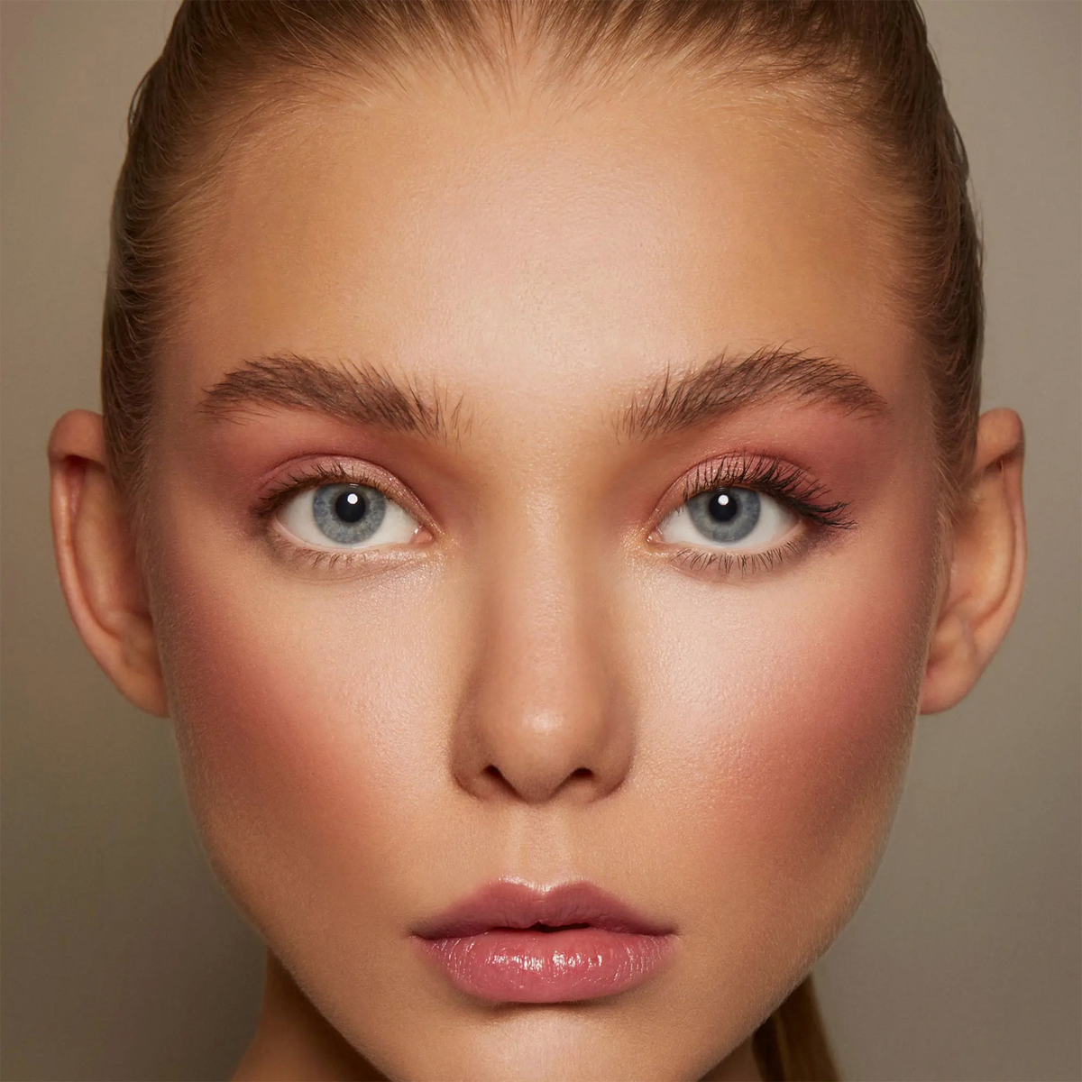 Nahaufnahme einer Frau mit blauen Augen, glänzenden Lippen, natürlichem Make-up und glatter, strahlender Haut, die die Emphasize Mascara von Mesauda Beauty trägt.