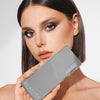 Frau mit glattem braunem Haar hält die silbern glänzende ARCHETYPE Makeup-Palette von Mesauda Beauty an ihr Gesicht.