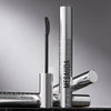 Eine silberne Tube Mesauda Beauty Femuline™ Mascara mit einer gebogenen Bürste wird auf einer reflektierenden Oberfläche präsentiert.