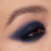 Nahaufnahme eines Auges mit intensivem, mattem blauem Smokey-Eye-Make-up und definierten Wimpern auf heller Haut.