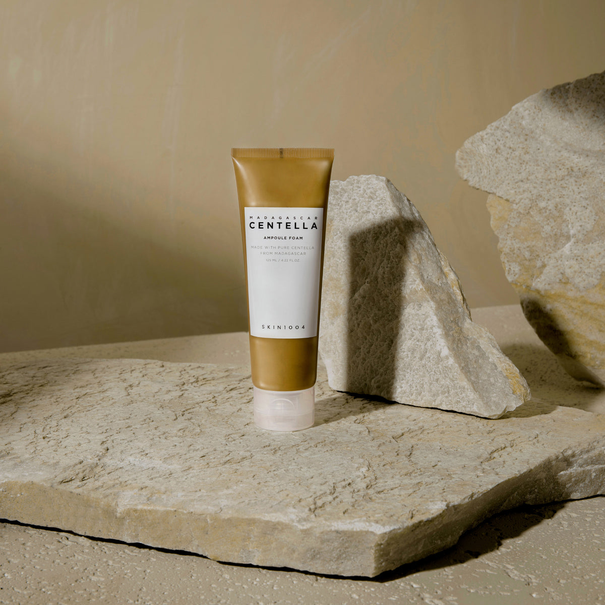 Eine Tube Madagascar Centella Ampoule Foam steht auf einer Steinoberfläche mit Felsen im Hintergrund.