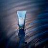 Die Tube Centella Hyali Cica Sleeping Pack steht auf plätscherndem blauem Wasser, um das sich Licht und Schatten spiegeln.