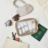 Reiseutensilien auf einem Bett: Sonnenbrille, Augenmaske, koreanischer Reisepass, Kulturbeutel, Kosmetiktasche und das Madagascar Centella Travel Kit.