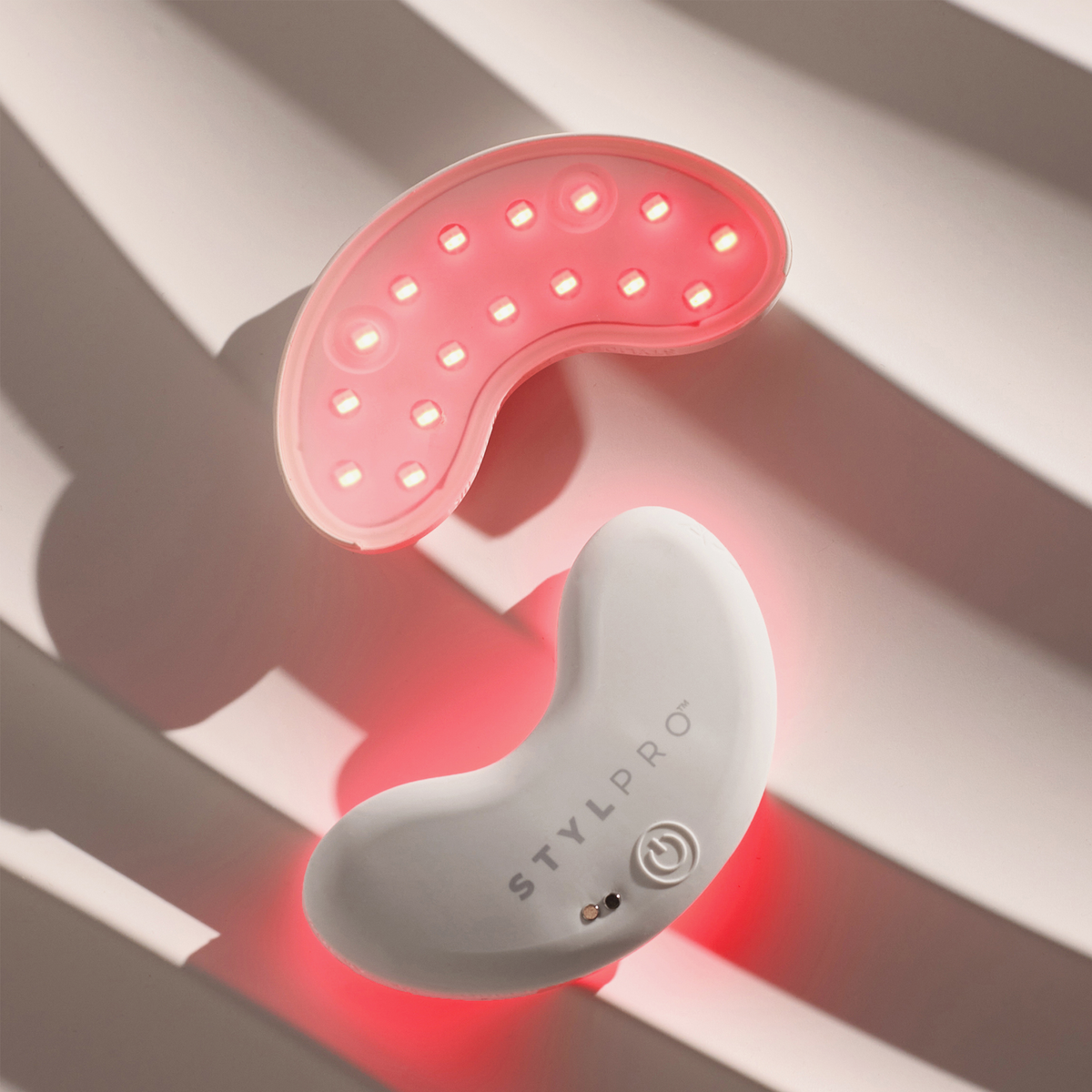STYLPRO LED Patch Duo in Weiß und Rosa, bohnenförmig mit roten LEDs, abgebildet vor einem leicht gewellten Hintergrund.