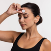 Eine Frau in einem schwarzen Tanktop hält das STYLPRO LED Spot & Blemish Patch, einen kleinen weißen Behälter, mit geschlossenen Augen an ihre Stirn.