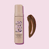Eine Flasche One Night Only Tan Instant Wash Off neben einem braunen Abstrich des Produkts vor einem rosa Hintergrund.