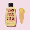 Eine gelbe Flasche Rapid Face Tanner von The Fox Tan ist neben einem Abstrich des Produkts auf einem rosa Hintergrund abgebildet.