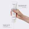 Eine Hand hält eine Tube PHA Soft Peeling Cleanser mit Etiketten, auf denen die Inhaltsstoffe angegeben sind: 5 % Gluconolacton und 2 % Salicylsäure.