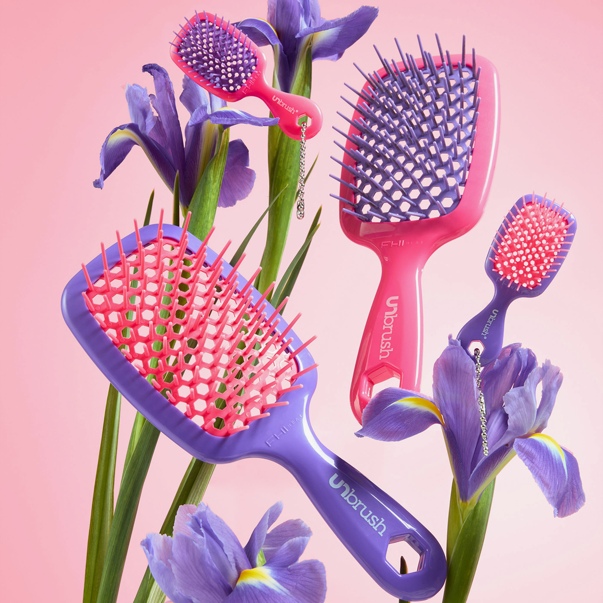 Zwei belüftete Haarbürsten der Marken UNbrush und Super Mini Set Neon Purple in den Farben Neon-Lila und Rosa sowie zwei kleinere, dazu passende Reisebürsten, eingebettet in Irisblüten.