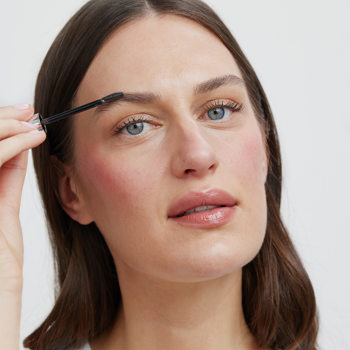 Eine Frau, die den XLASH Brow Booster mit einer Spoolie-Bürste aufträgt.