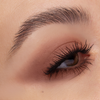 Nahaufnahme eines braunen Auges mit dichten Brauen und langen Wimpern, betont durch braunes Lidschatten-Make-up, das mit Cupid’s Arrow Longwear Stylo erstellt wurde.