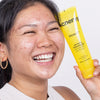 Eine Person schaut lächelnd in die Ferne und hält eine 150 ml Tube Zitclean an ihre linke Wange.