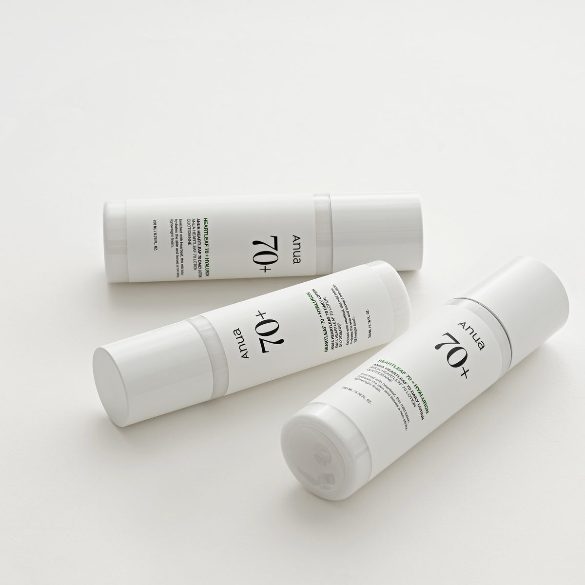 Drei weiße Hautpflegeflaschen mit der Aufschrift „Heartleaf 70 Daily Lotion“ sind diagonal auf einem hellen, neutralen Hintergrund angeordnet.