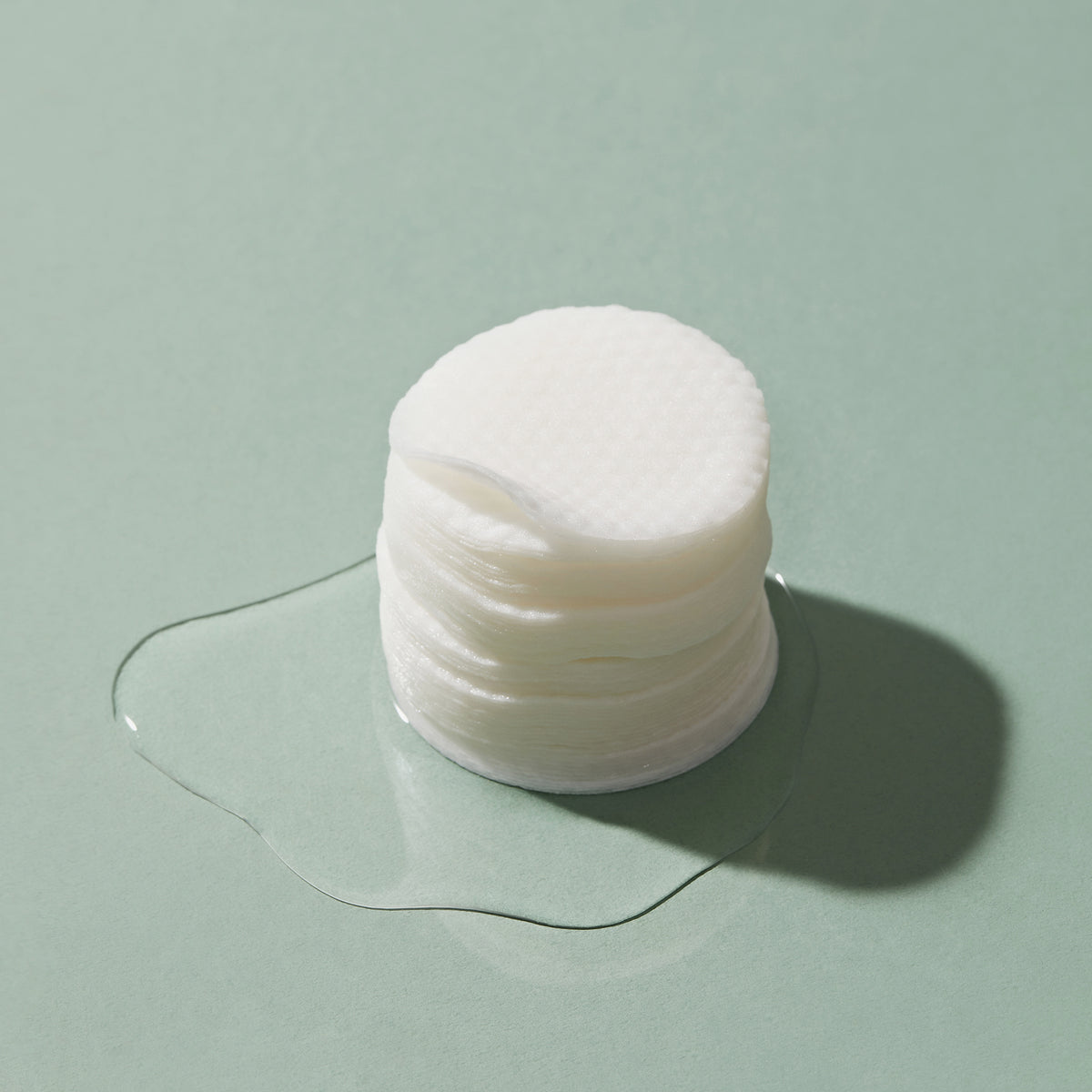 Ein Stapel Heartleaf 77 % Tonerpads liegt auf einer grünen Oberfläche, umgeben von einer kleinen Flüssigkeitslache.