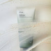 Eine Tube Heartleaf Quercetinol Pore Deep Cleansing Foam liegt auf einer cremigen, strukturierten Oberfläche mit sichtbaren Peelingpartikeln.