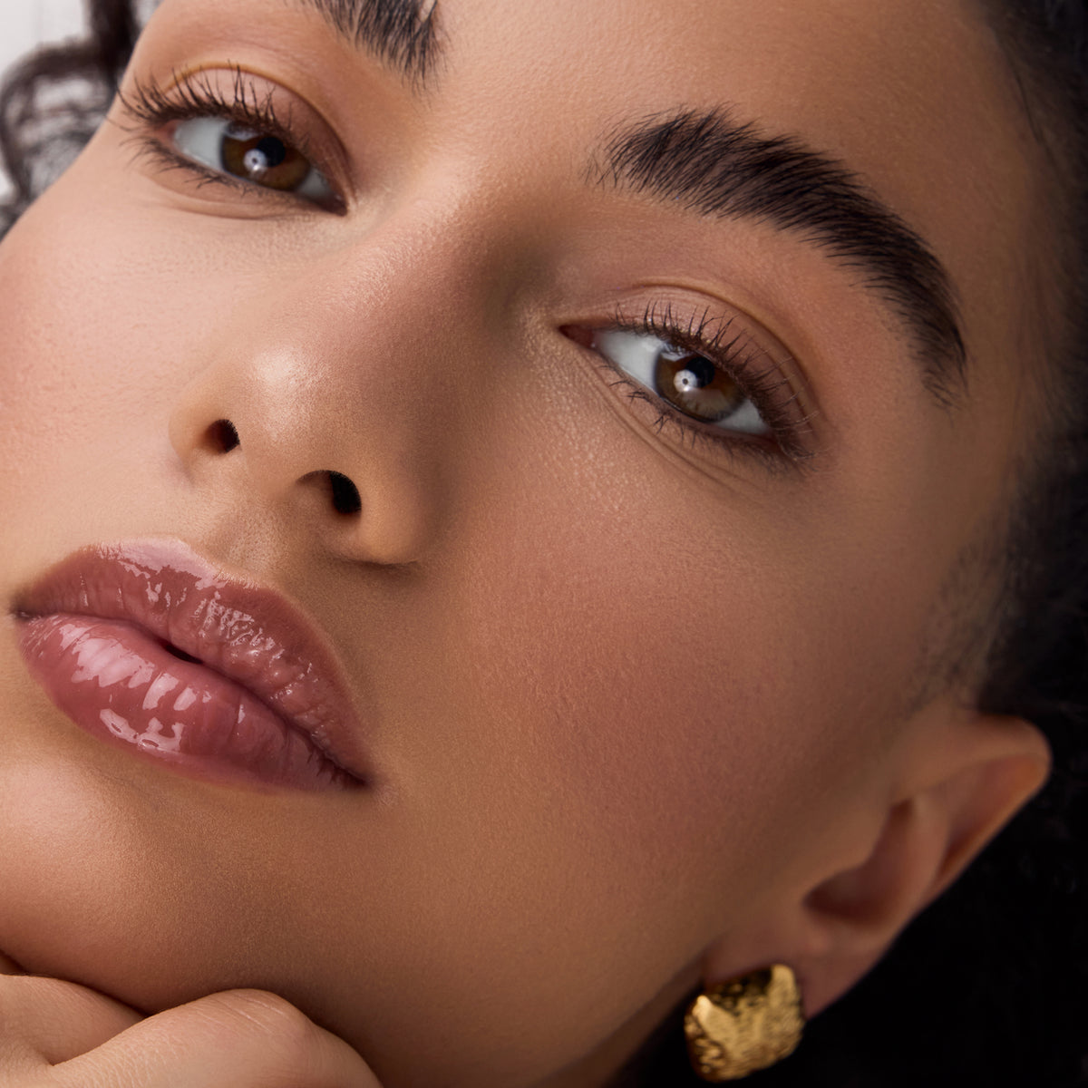 Nahaufnahme eines Gesichts mit glänzenden, braun-beigen Lippen, betont durch Catrice Colour Cushion Juicy Lip Oil für ein elegantes, gepflegtes Finish.