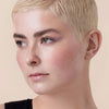 Eine Person mit kurzem blonden Pixie-Haarschnitt trägt den Soft Glam Filter Fluid und fliederfarbenen Eyeliner.