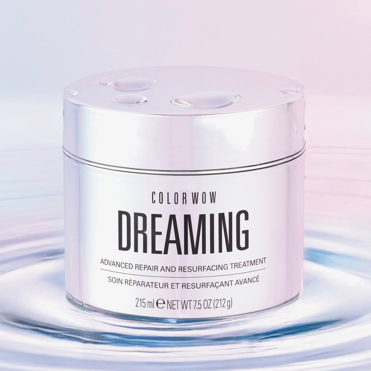 Ein silbernes Gefäß mit Color Wow Dreaming Treatment ruht auf plätscherndem Wasser vor einem weichen pastellfarbenen Hintergrund.