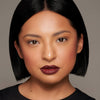 Frau mit glattem schwarzem Bob trägt Danessa Myricks Beauty Dewy Cheek & Lip Palettes, kräftige Lippen und neutrales Make-up.