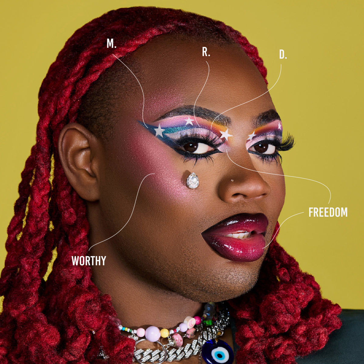 Eine Person mit dunklem Teint mit auffälligem Make-up aus der Love is Love-Palette und roten Zöpfen.