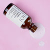 Eine geöffnete Flasche Power Peptides-Serum liegt auf rosa Oberfläche, daneben ist Flüssigkeit verschüttet.