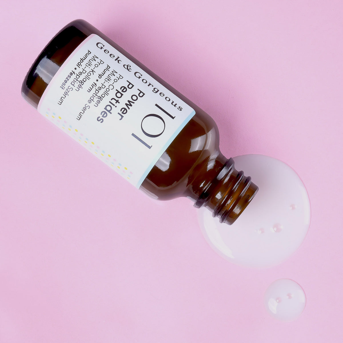 Eine geöffnete Flasche Power Peptides-Serum liegt auf rosa Oberfläche, daneben ist Flüssigkeit verschüttet.