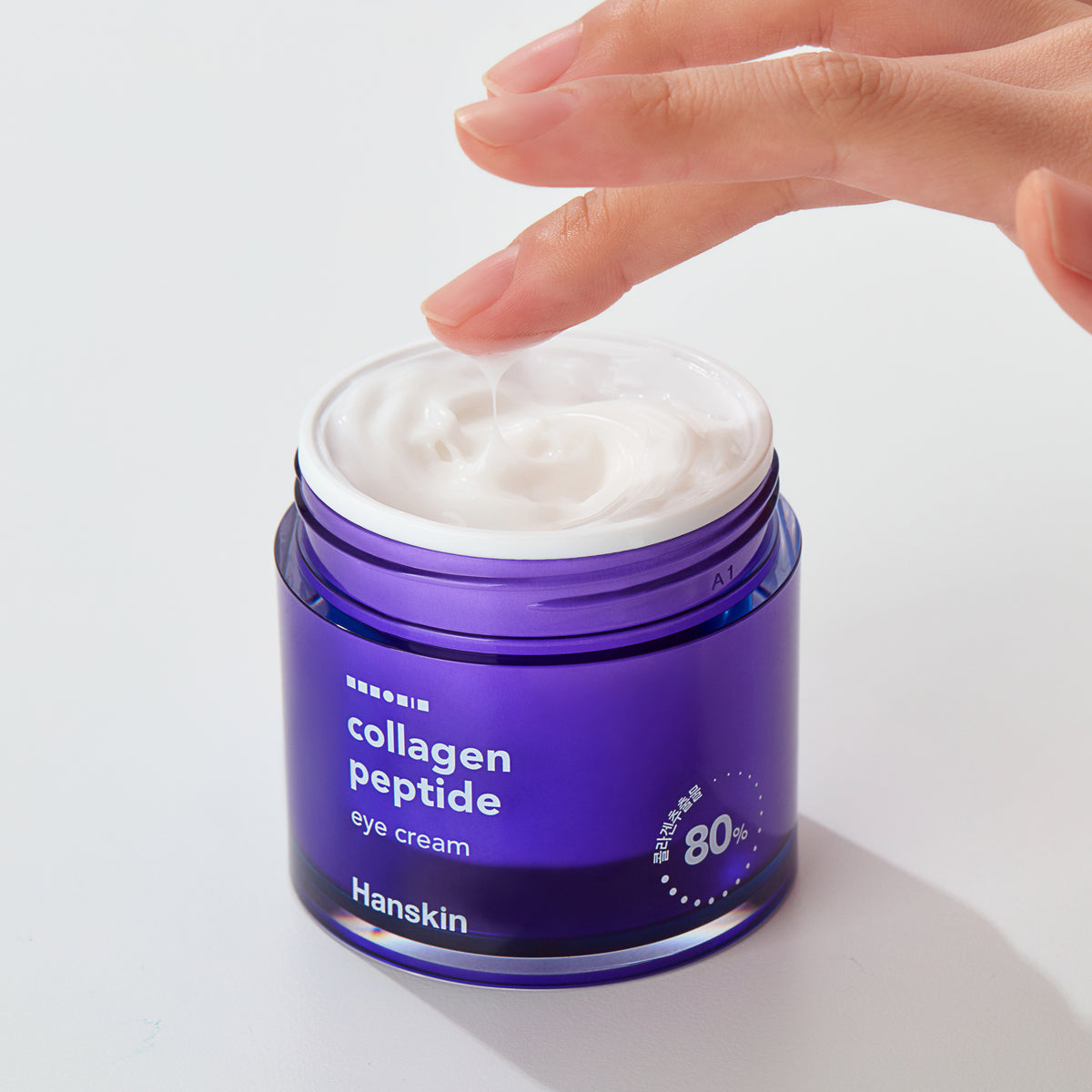 Eine Hand schöpft weiße Collagen Peptide Eye Cream aus einem lila Tiegel.