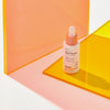 Eine Flasche Hanskin Vitamin C Glow Serum steht auf einer gelben Acryloberfläche mit rosa Hintergrund.