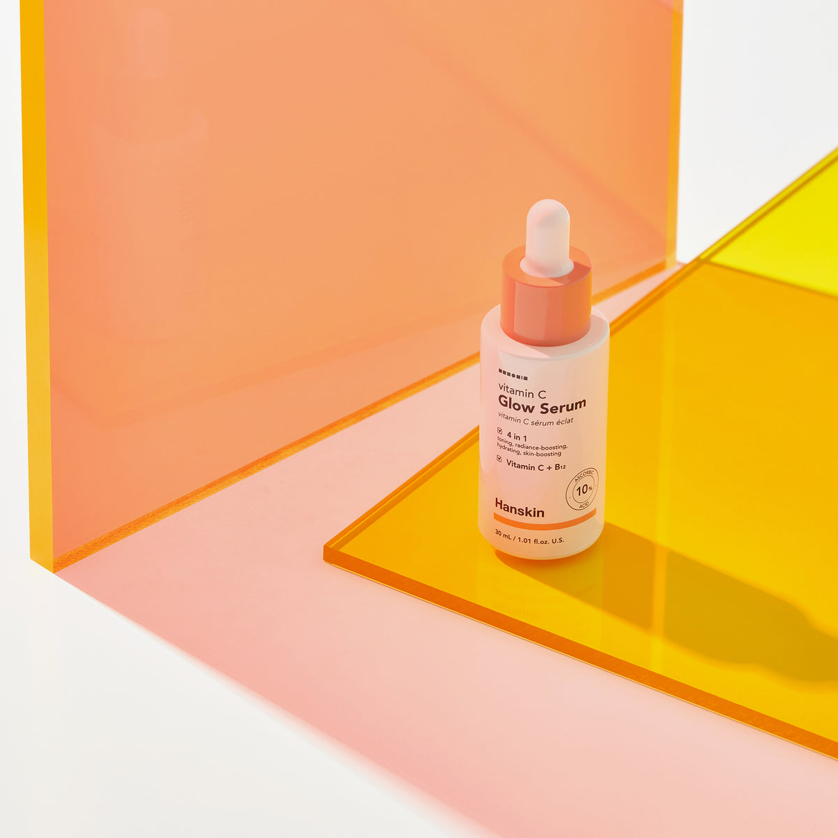 Eine Flasche Hanskin Vitamin C Glow Serum steht auf einer gelben Acryloberfläche mit rosa Hintergrund.
